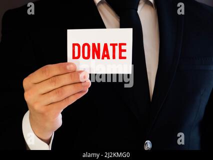 The word donate medical concept written in red letters on a white piece of paper in the hands of a businessman.