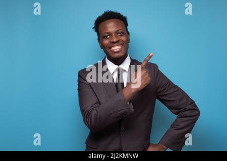 Smiling african man wearing suit looking at camera pointing aside giving advice. Portrait of black confident man at home. Successful entrepreneur feel Stock Photo