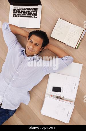 Taking a break from his work. High angle shot of a young businessman lying on his home floor surrounded by work. Stock Photo