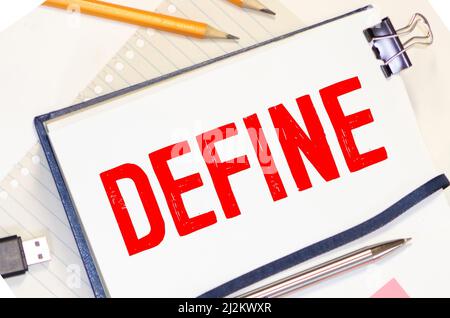 The word DEFINE is written in a notebook near multi-colored pencils and buttons on a wooden background. Stock Photo
