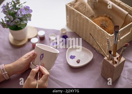 Womens hands paint a white flower ceramic pot on the table Stock Photo