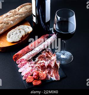 Spanish snack with chorizo, salchichon, jamon, fresh baguette and a glass of red wine. Stock Photo