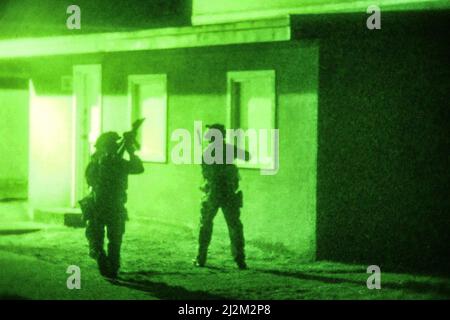 Green Berets with 2nd Battalion, 1st Special Forces Group (Airborne), inspect a building on their way to an objective during a training exercise at Camp Rilea Armed Forces Training Center, March 25, 2022. Following training with the U.S. Coast Guard, the Green Berets completed a training exercise including a water movement to an objective for a simulated night raid. Stock Photo