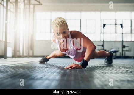 Excuses dont burn calories. Shot of a young attractive woman doing push ups with one hand at the gym. Stock Photo
