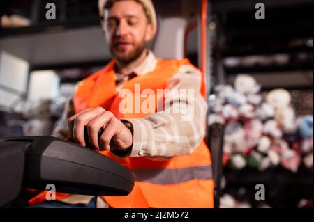 Young forklift driver sitting in vehicle in warehouse smiling. Focus on hand. Stock Photo