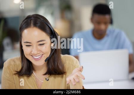 Our operators are well-prepared to handle your inquiries. Shot of a young businesswoman working in a call centre with her colleague in the background. Stock Photo