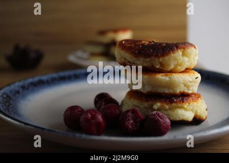 Three pancake cheesecakes lie a stack of slides on top of each other on a plate on a table with cherry cherry jam sauce. View from the side. Breakfast Stock Photo