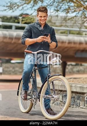 Life is like riding a bike, to stay balanced you must keep moving. Shot of a young male student using his mobile phone while cycling on campus. Stock Photo