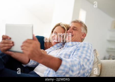 Lets show the world what love looks like. Cropped shot of a mature couple taking a selfie on a digital tablet at home. Stock Photo