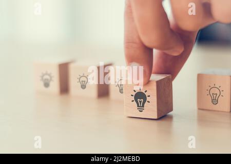 Idea and creativity concept. Male hand holds wooden cube with light bulbs icon on light background. Teamwork brainstorming ideas, evaluation and selec Stock Photo