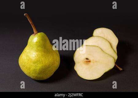 Two ripe green pears on a dark background, late november pear variety. Whole pear and sliced Stock Photo