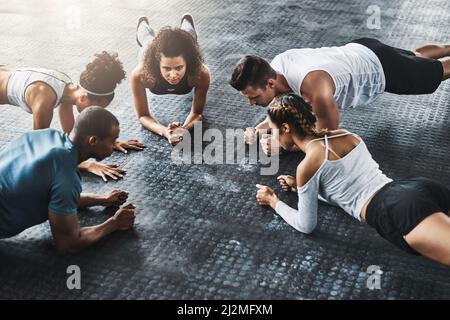 Planking - so simple, so effective. Shot of a group of young people doing planks together during their workout in a gym. Stock Photo