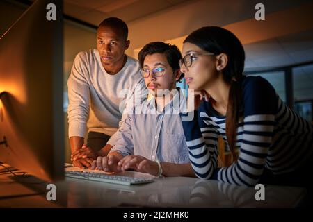 Getting work done together. Shot of computer programmers working together late in the office. Stock Photo