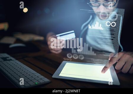 Credit card fraud - its a risk and reality. Shot of a young hacker using a digital tablet to commit credit card fraud in the dark. Stock Photo