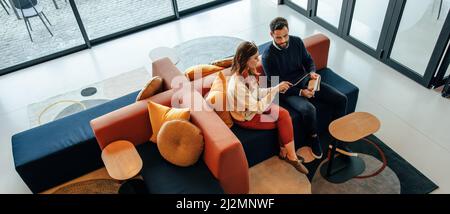 High angle view of two businesspeople working in an office lobby. Two modern businesspeople using a digital tablet while having a discussion. Two youn Stock Photo