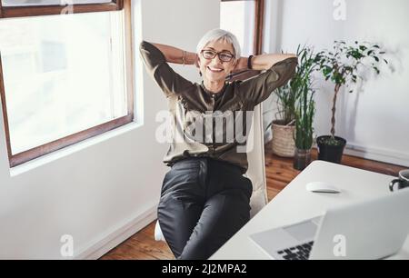 I crush deadlines. High angle portrait of an attractive mature businesswoman sitting with her hands behind her head in the office. Stock Photo