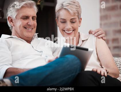 Is this what the kids are watching. Shot of a mature couple using a digital tablet at home on the sofa together. Stock Photo