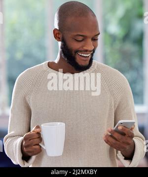 This app is so convenient. Shot of a young man drinking coffee while using a phone at home. Stock Photo