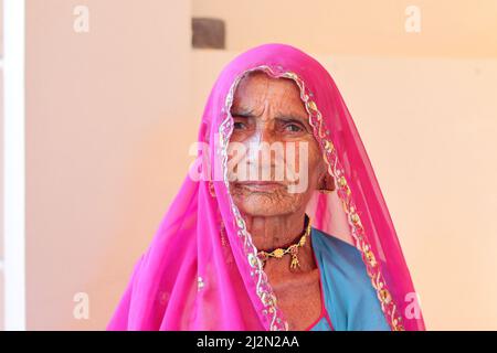 Pali Rajasthan , India - October 23, 2021. Close-up portrait photo of An indian elderly woman sitting in a pinkish red veil. Indian village Stock Photo