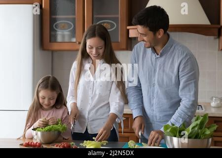 Happy family couple and sweet little daughter preparing ingredients Stock Photo