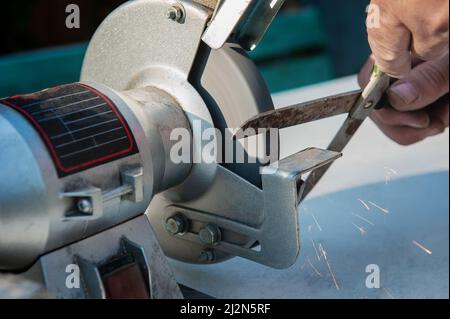 Manual sharpening of scissors using hand tools. Circumcised Hands Of An Unknown Person Sharpening Scissors On A Typewriter. man sharpens scissors Stock Photo