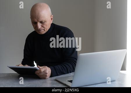 Unhappy depressed senior male sitting at desk with laptop, having frustrated stressed look Stock Photo