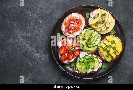 Assorted sandwiches with soft cheese, vegetables and fruits on a dark background. Stock Photo