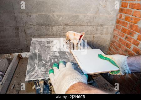 hands of a locksmith in special clothes works in the production of home repairs. Processing of ceramics with an angle grinder. Cuts ceramic tiles with Stock Photo
