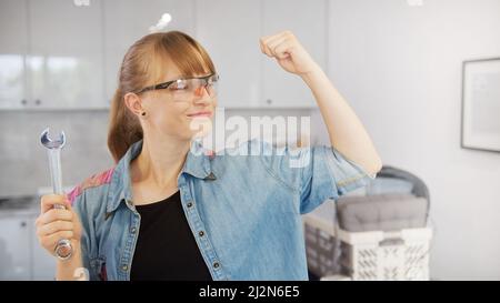 Strong, confident, independent red-haired caucasian woman holding a wrench in one hand and flexing her muscles. High quality photo Stock Photo