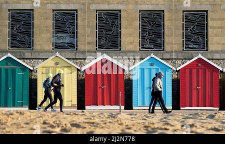 People make their way past beach huts on Boscombe beach in Dorset. Picture date: Sunday April 3, 2022.