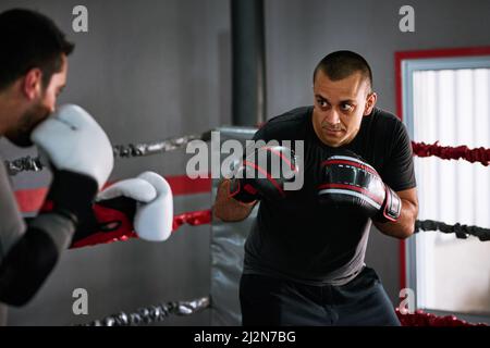 Simulating real fighting situations. Cropped shot of two young male athletes sparring in a boxing ring. Stock Photo