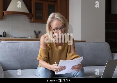 Serious mature 50s landlady woman un glasses reading domestic papers Stock Photo
