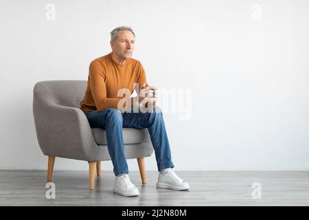 Man having rest at home sitting on chair, drinking coffee Stock Photo