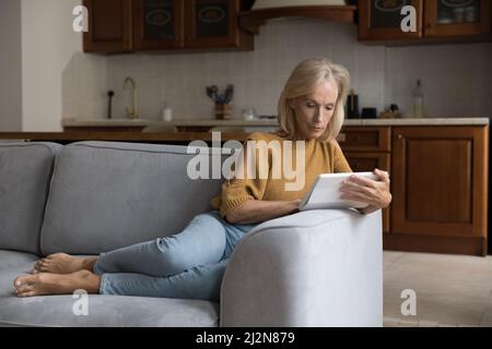 Focused middle aged customer lady using tablet computer at home Stock Photo