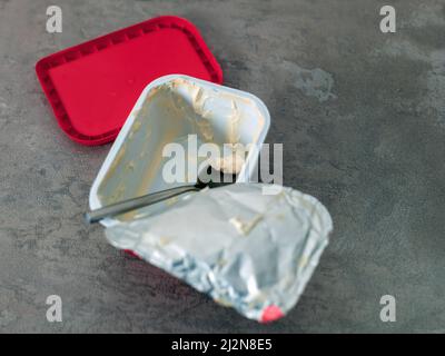 an empty plastic box of processed cheese or spread and spoon abandoned on a table Stock Photo