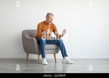 Smiling mature man waving hand using mobile phone Stock Photo