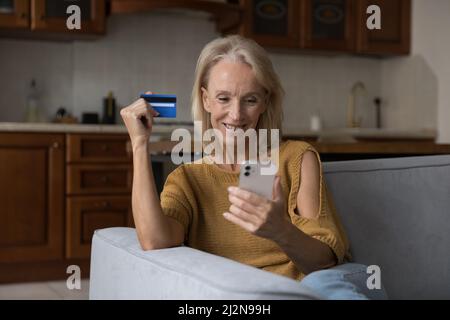 Happy mature customer lady using credit card, mobile phone Stock Photo