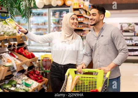 Muslim Spouses Doing Shopping Taking Vegetables From Shelf In Supermarket Stock Photo