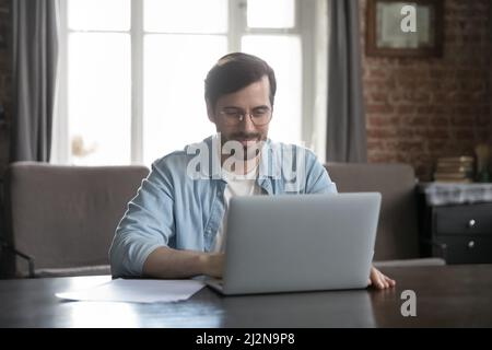 Happy millennial freelance employee man using computer at home office Stock Photo
