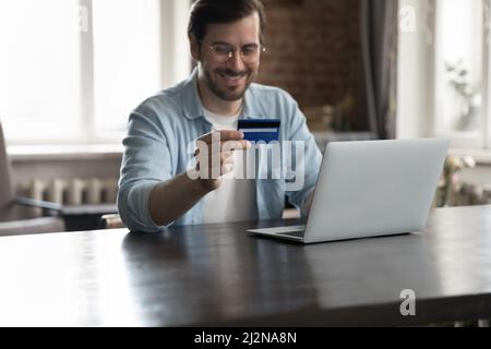 Happy cheerful bank customer man using laptop and credit card Stock Photo