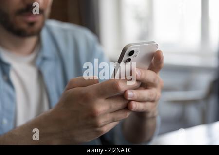 Millennial Caucasian man sitting at table, holding cellphone, Stock Photo
