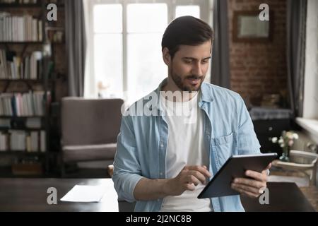 Positive focused millennial business man using online app on tablet Stock Photo