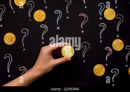 Hand holding Bitcoin virtual money against blackboard with question marks. Digital currency concept Stock Photo