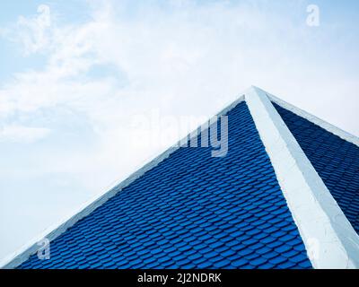 Arrangement of blue house roof tiles in white cement edge frame on the top on blue sky background with copy space. Stock Photo