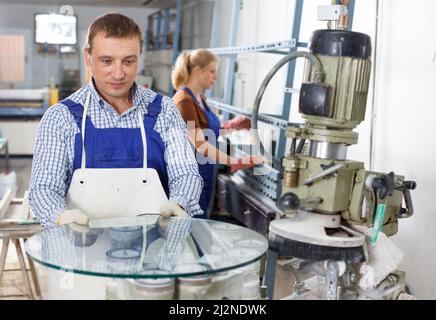 Man working on curved glass beveling machine Stock Photo