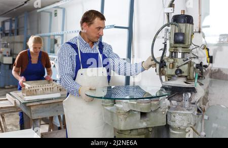 Man working on curved glass beveling machine Stock Photo
