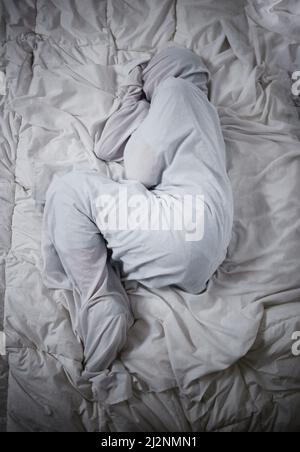 Mental health problems dont define who you are. Shot of a unrecognizable man laying under the covers in a mental asylum. Stock Photo