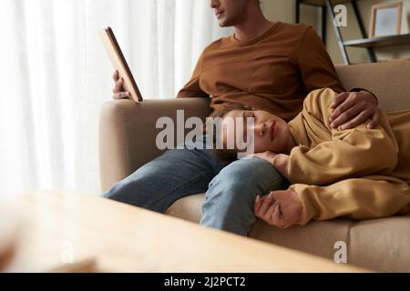 Tired young woman fell asleep with head on laps of boyfriend who is reading article on tablt computer Stock Photo
