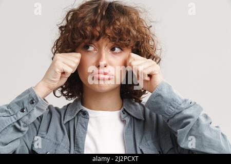 Unhappy ginger woman in shirt crying and looking aside isolated over white background Stock Photo
