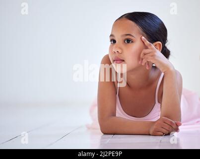Dreaming about dancing on the big stage. Shot of a little girl looking thoughtful while lying on the floor in a ballet studio. Stock Photo